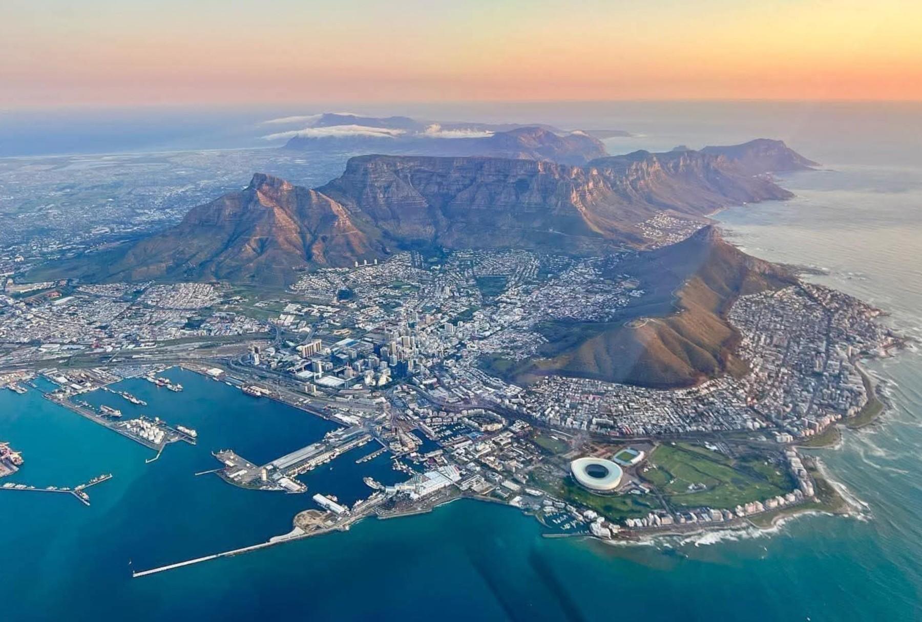 Aerial view of Cape Town at sunset, showing Table Mountain, Lion's Head, the city centre, the harbour and Cape Town Stadium.